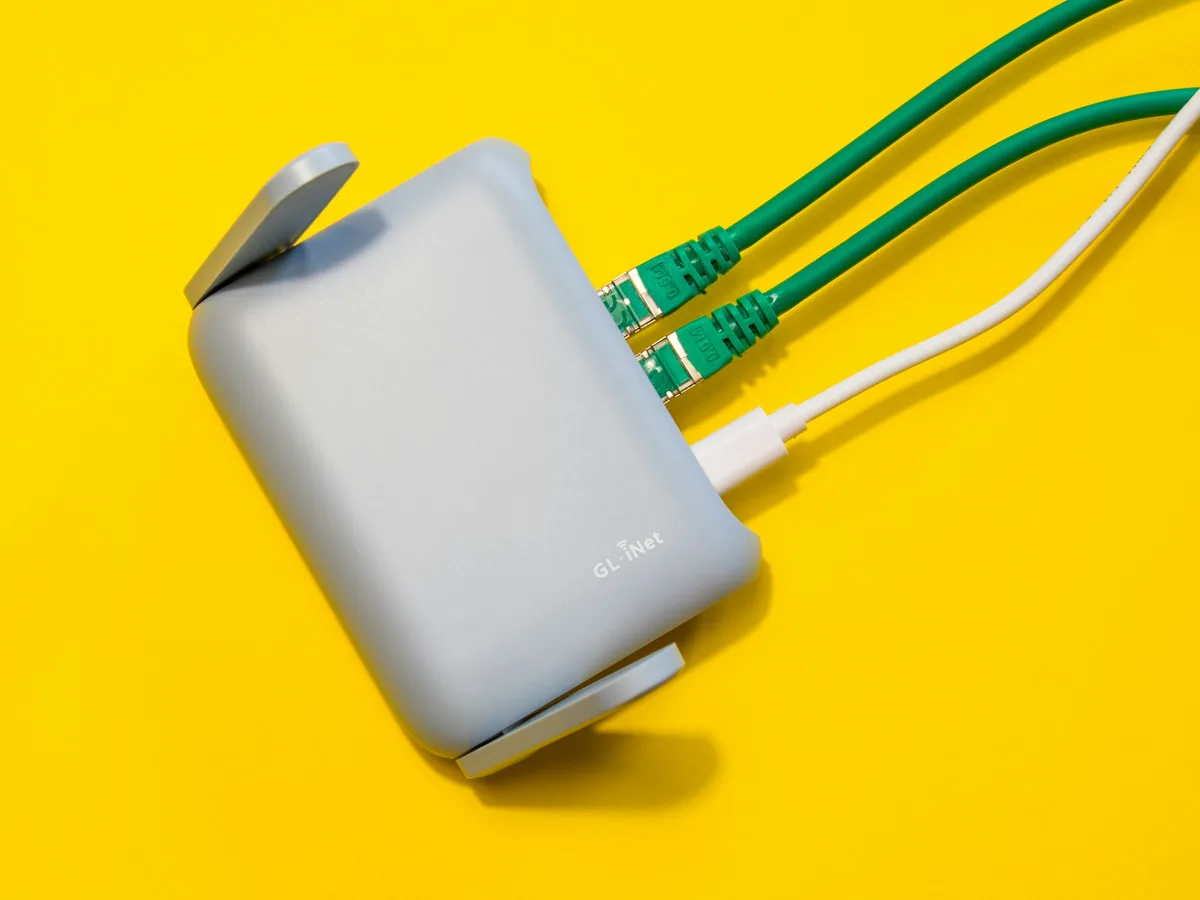 A compact Wi-Fi router with green and white network cables plugged into its ports